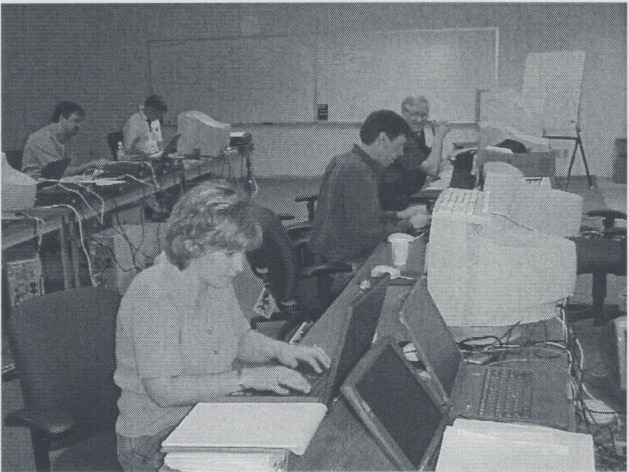 A black and white image of people sitting at desktop computers