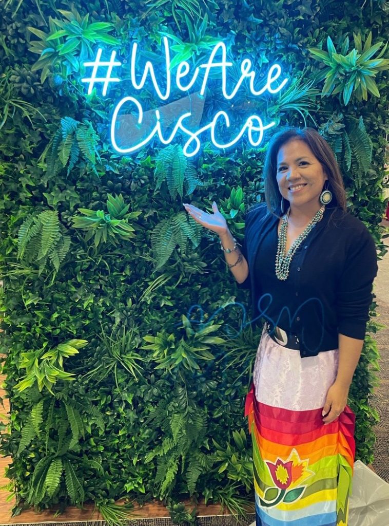 A woman standing next to a Neon We Are Cisco sign