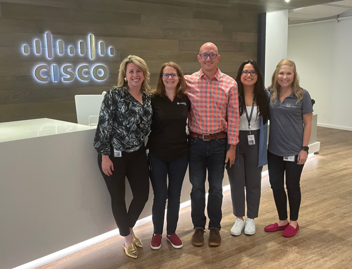 Mike Rausch stands and smiles with four of his coworkers. They are in an office setting with the Cisco logo in the background.