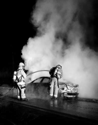 Two firefighters putting out the fire in a burning car. 