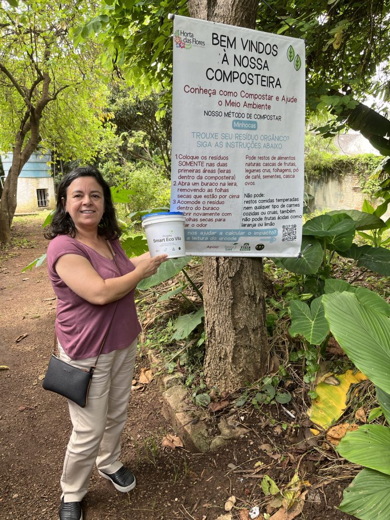 A woman holding a bucket near a sign about composting in Spanish.