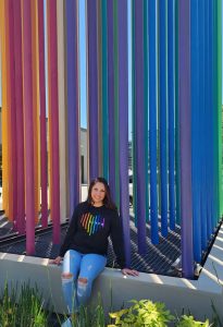 Woman seated in front of rainbow art sculpture wearing Cisco Pride shirt.