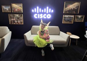 Little girl dressed as green fairy sitting on couch under Cisco logo neon sign.