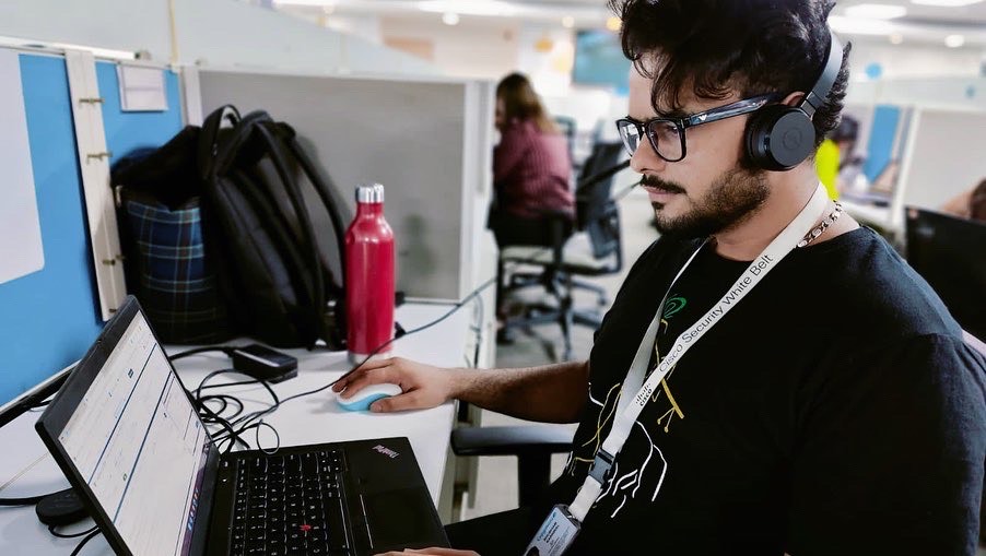 Shubham sitting at desk on laptop wearing headphones.