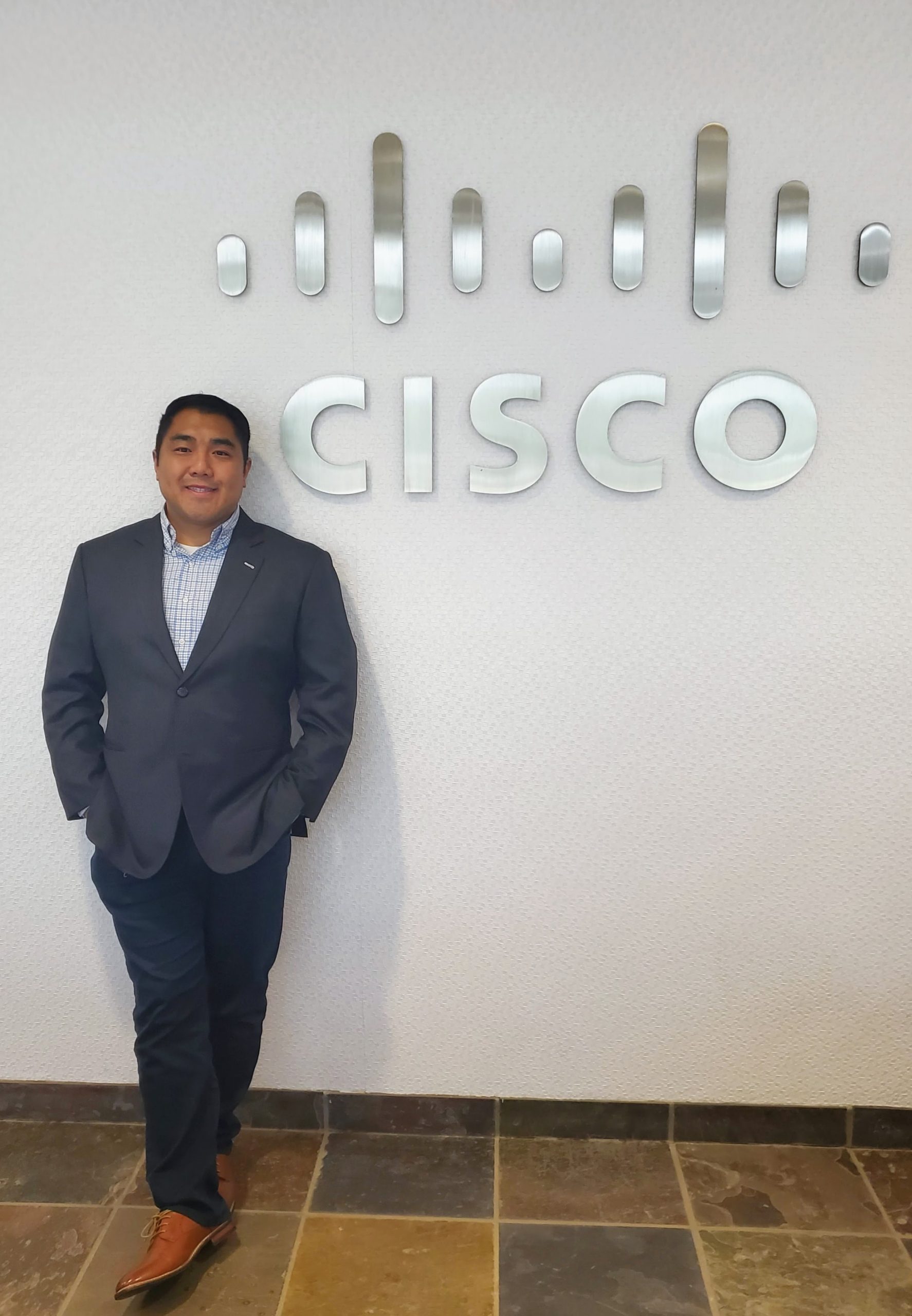 Jonathan wearing a suit and standing next to a Cisco sign.