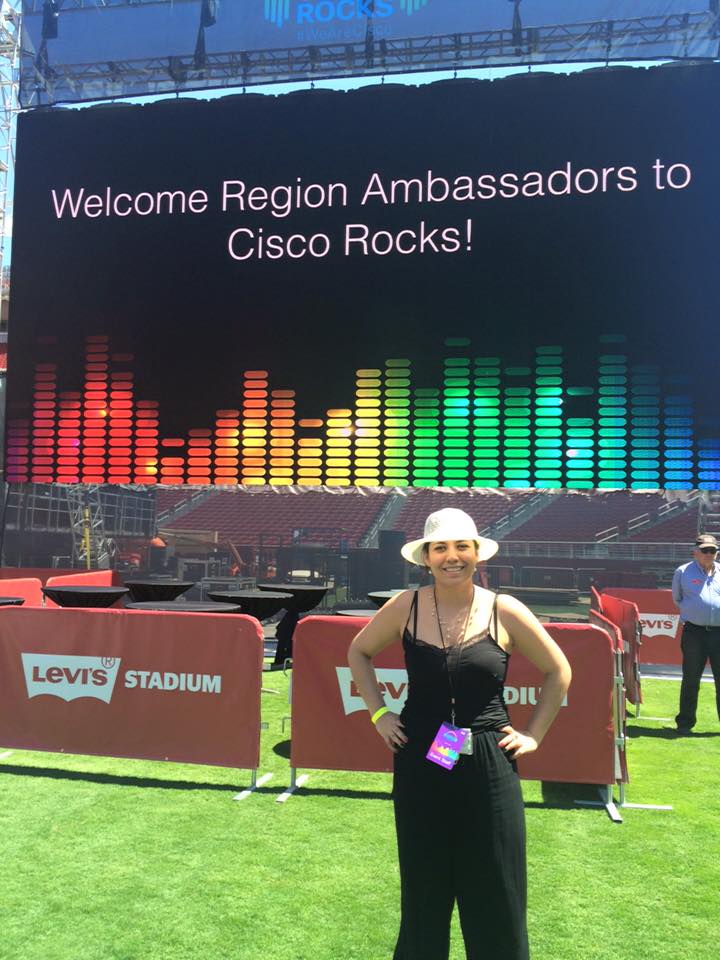 Carmen standing in front of a wall that reads, "Welcome Region Ambassadors to Cisco Rocks!"