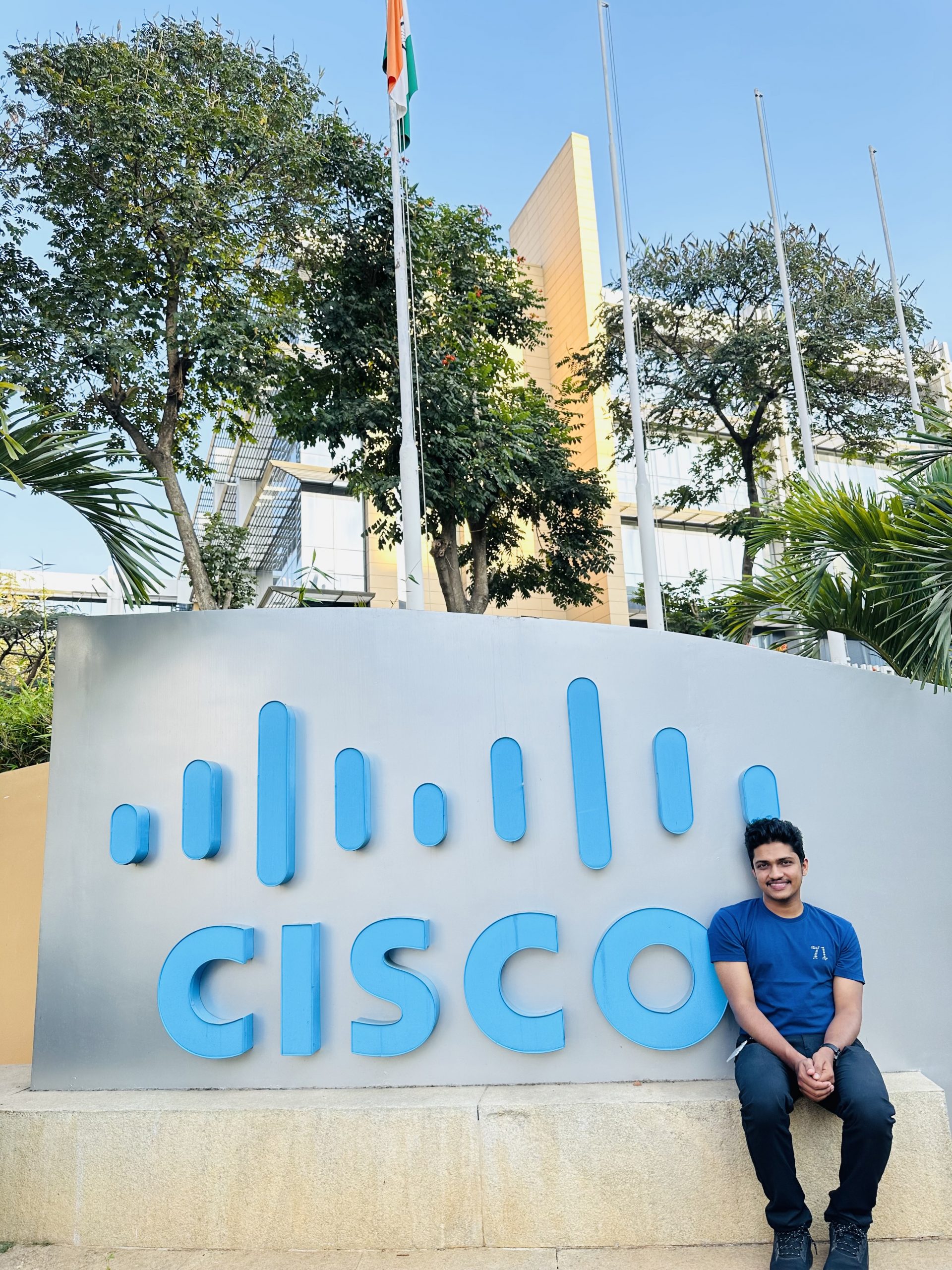 Najid sits on the Cisco sign in front of the buildings on the campus in Bangalore