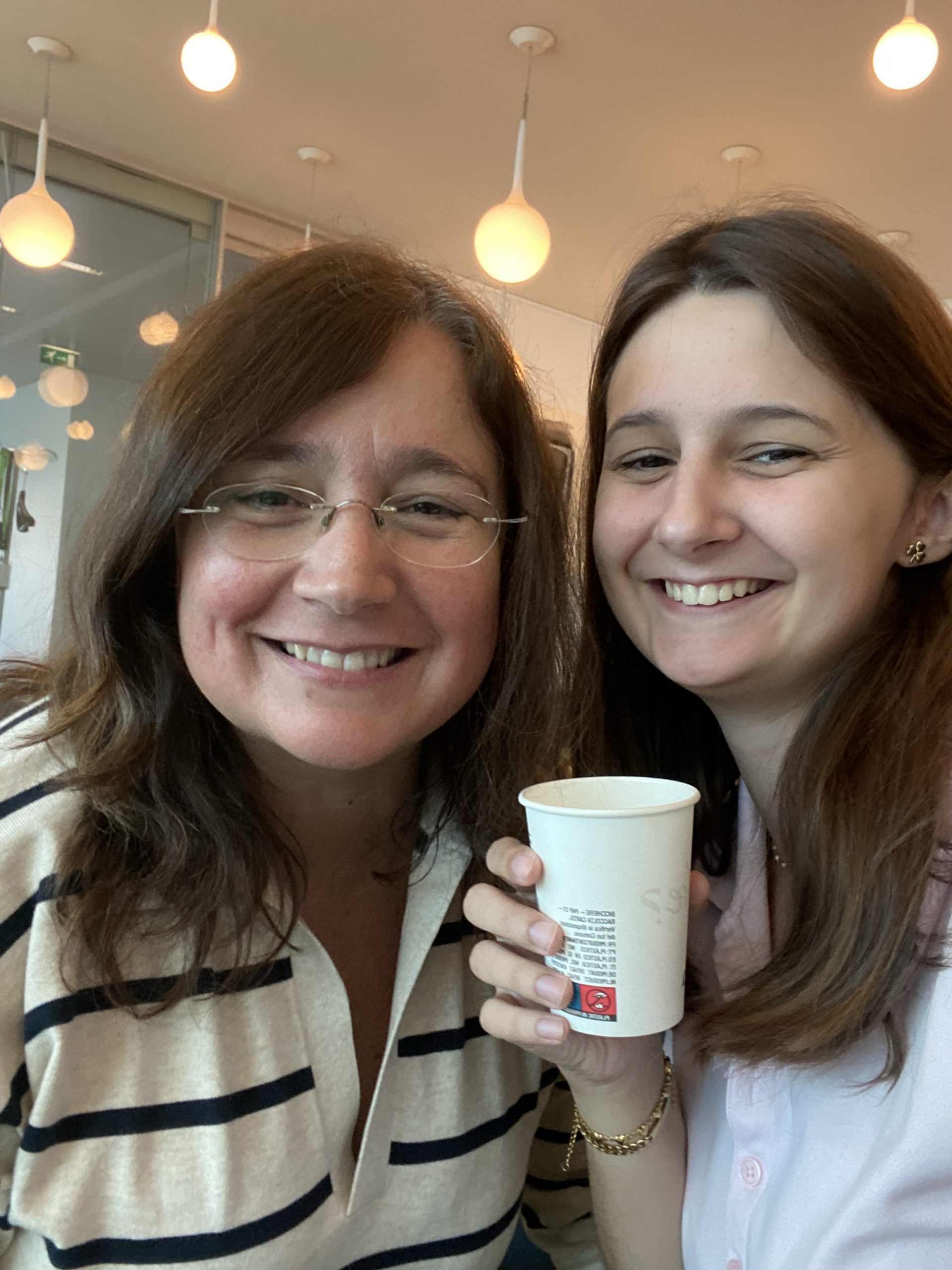 Twopeople smiling while one holds up a paper cup.