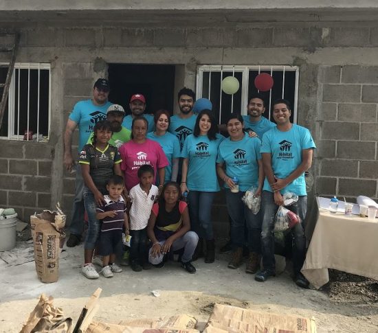 A group of volunteers stand together in front of a building renovation.