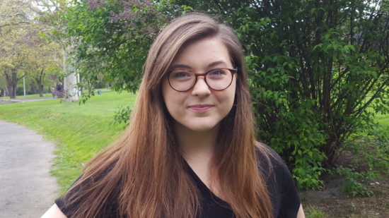 Chloe, wearing glasses, smiles outdoors.