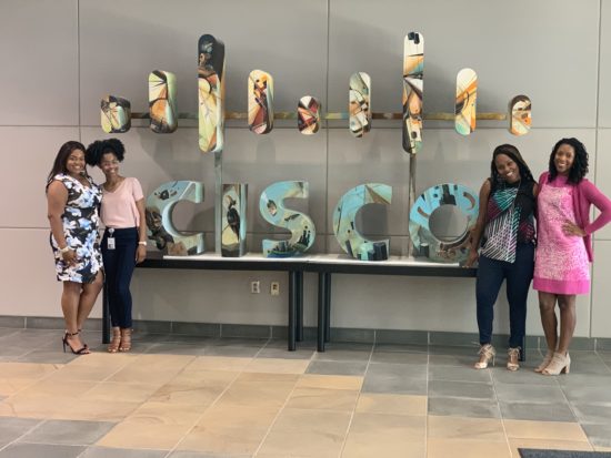 Makeda stands smiling with her peers and friends next to a Cisco sign in RTP.