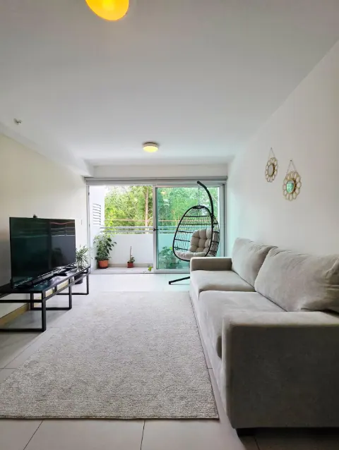 Living room with sofa, TV, and balcony overlooking the trees