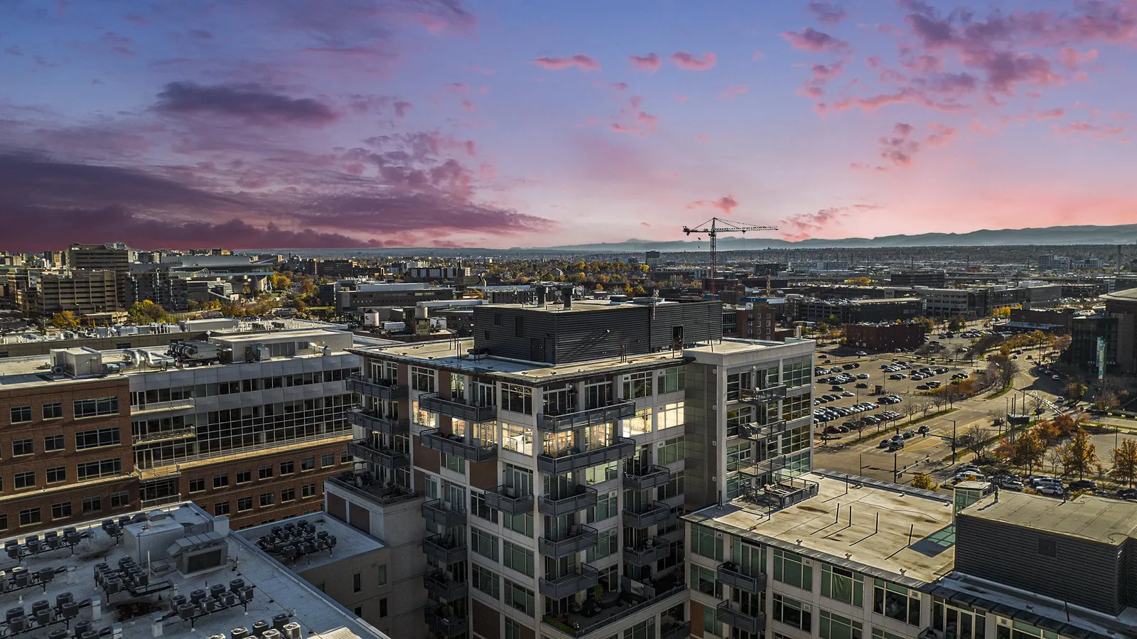 Aerial view of an urban district at dusk, with modern buildings, a construction crane, and distant hills.