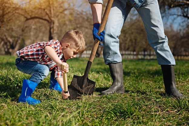 A child uses a little shovel to help his parents dig in the yard.