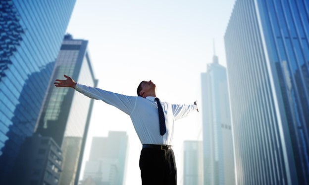 A happy young professional stretches their arms toward the sky, surrounded by buildings in a city.