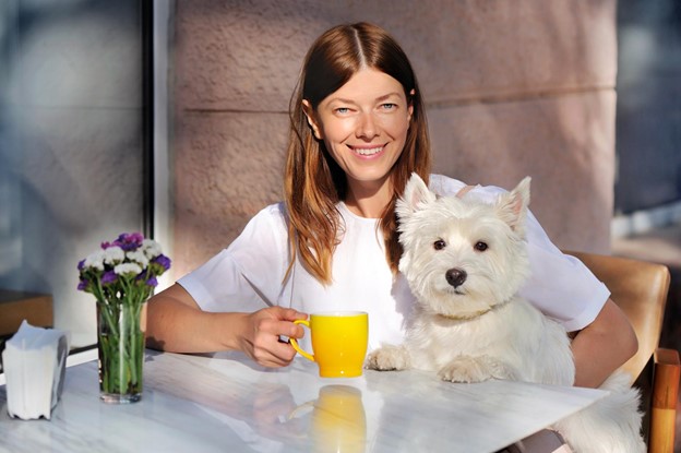 A person sips some coffee while holding their dog at a pet-friendly cafe.