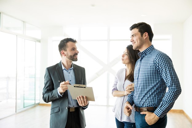 A young couple interviewing a real estate agent inside a brightly lit room of an open house.