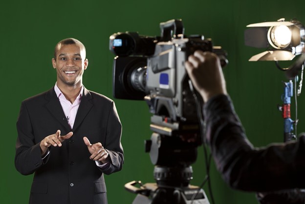 A person presenting in front of a TV camera and its operator.