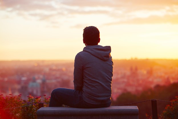 A person sits and thinks while watching the sunset fall over a city.