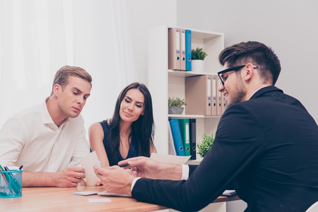 A smiling couple examines a mortgage contract with a real estate agent.