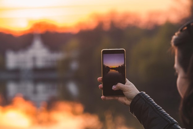 A person taking a picture of a sunset falling over a city on their phone.