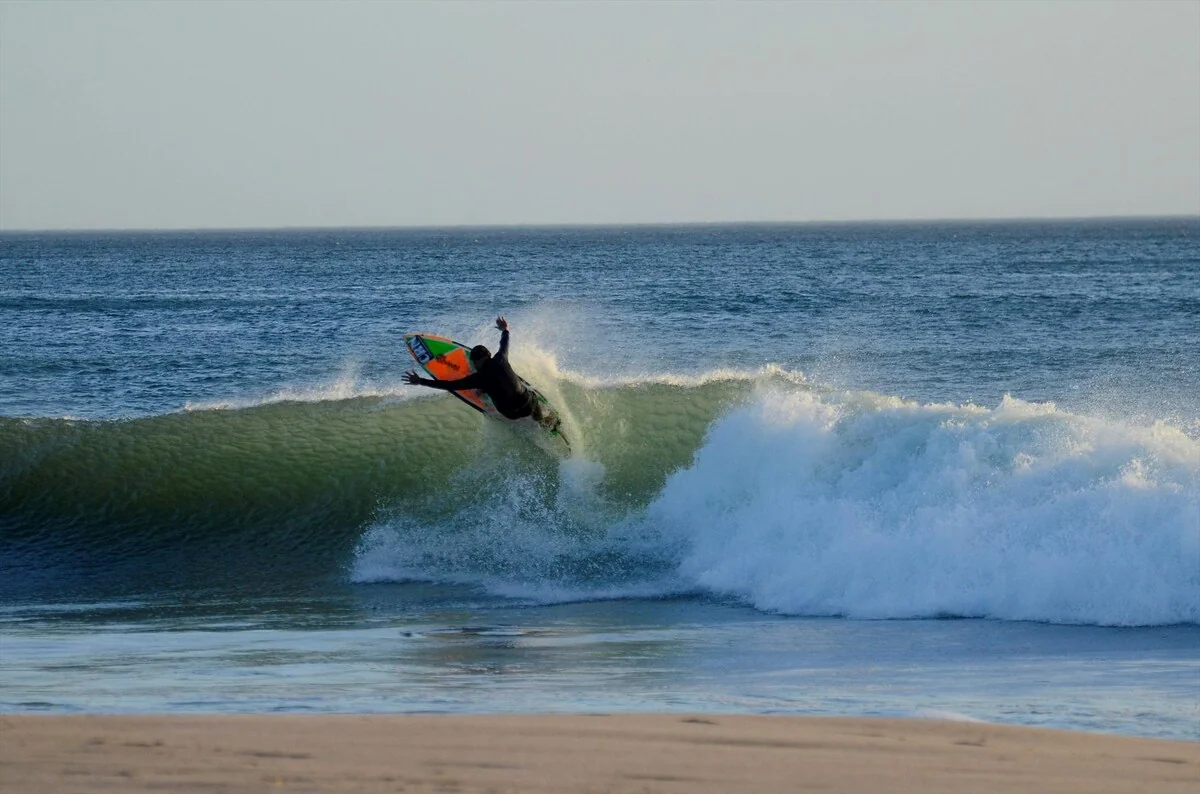 A surfer rides a breaking ocean wave near the sandy beach.