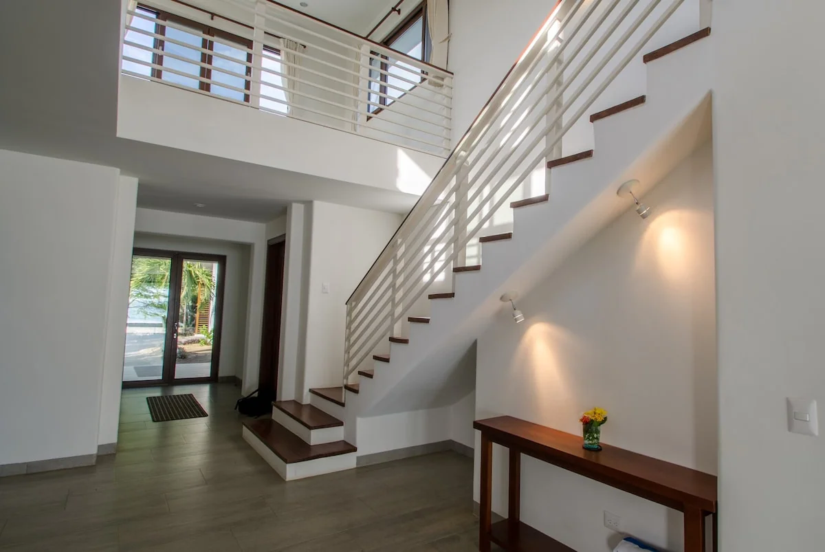 A bright modern entry hall features a staircase with white metal railings, wood steps, and a narrow console table.