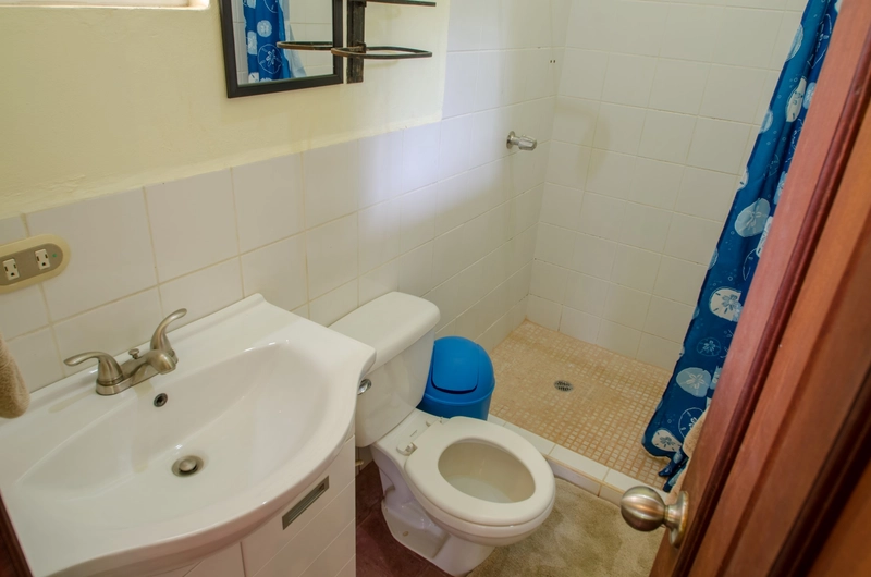 This image shows a small bathroom. On the left, there's a white sink with a stainless steel faucet. Below the sink, there's a cabinet for storage. Next to the sink is a white toile