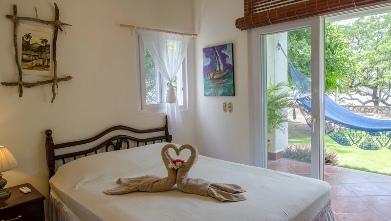 A cozy bedroom featuring a neatly made bed with creatively arranged towels forming heart shapes. The room is decorated with two wall pictures and receives ample natural light throu
