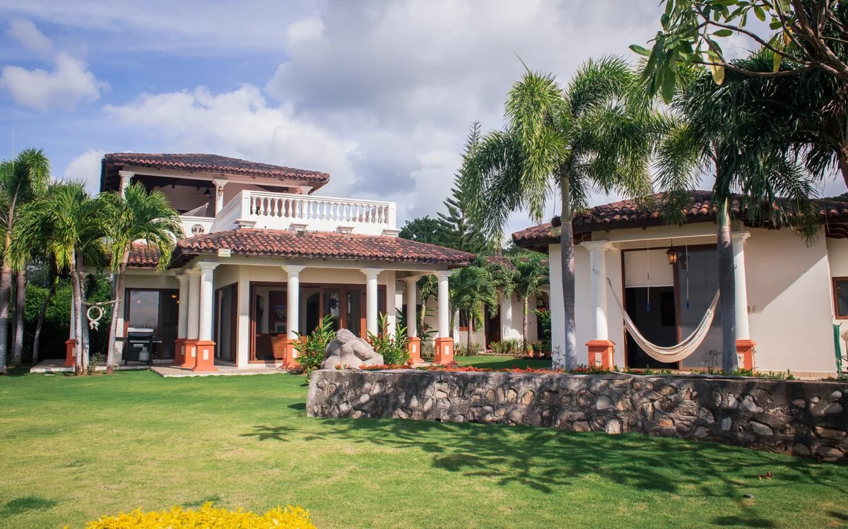 A bright tropical property with tiled-roof buildings, palm trees, a hammock, and a broad green lawn.