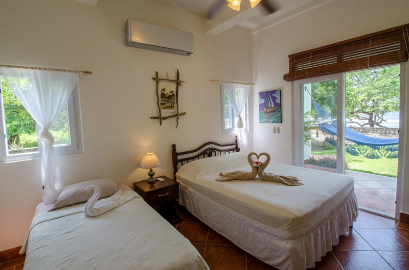 A bright bedroom featuring a twin bed and a double bed adorned with creatively folded towels in the shapes of a swan and two entwined hearts. The room includes a wooden nightstand 
