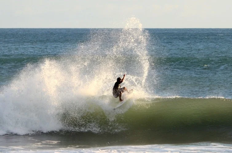 A surfer rides inside a breaking ocean wave surrounded by bright spray.