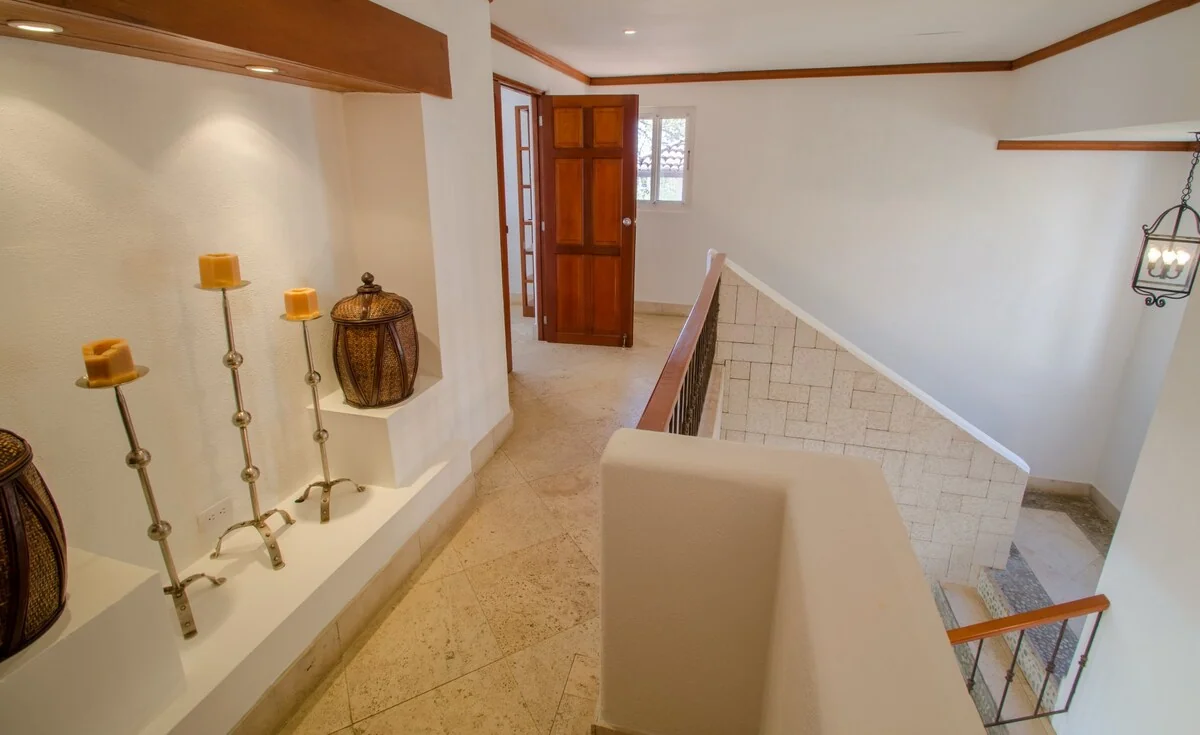 An interior landing shows an open wooden door, a tiled stairwell, decorative candles, a vase, and a hanging lantern.