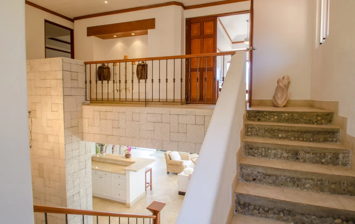 An interior staircase with stone-textured steps overlooks a bright lower-level kitchen and living area.