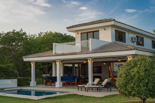 A two-story house with a covered patio, balcony, outdoor seating, and a small swimming pool surrounded by greenery.