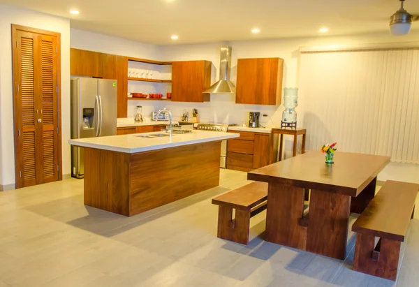 A bright open-plan kitchen and dining area features wooden cabinetry, a central island, and a dining table with benches.