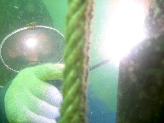 Bright Spark Indonesia underwater welding close-up with a gloved hand and a bright welding arc.