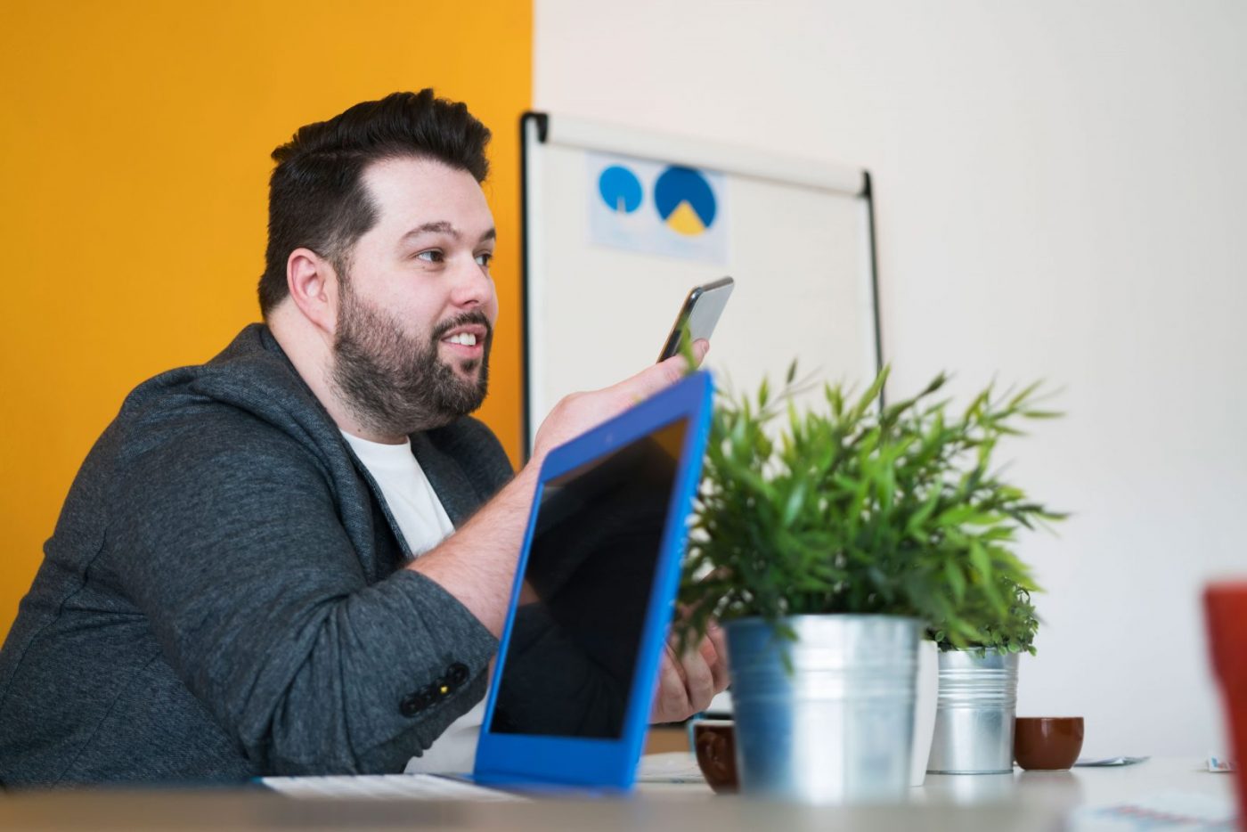Man sat in an office environment with an ipad in the foreground, he is looking at his phone.