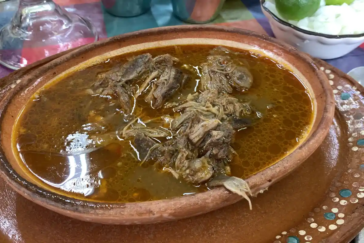 Birria de chivo servida sobre un plato de barro