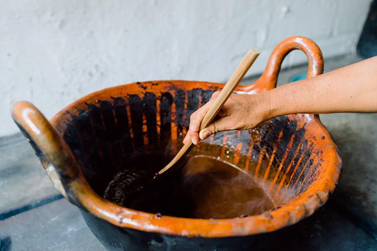 Mujer moviendo a una olla de barro con mole