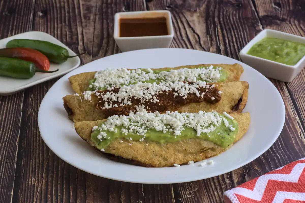 Quesadillas fritas con salsa verde y roja sobre una mesa de madera