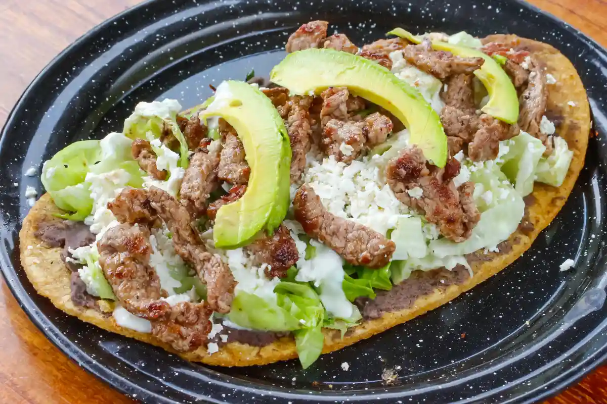 Huarache servido con aguacate, bistec, queso y crema
