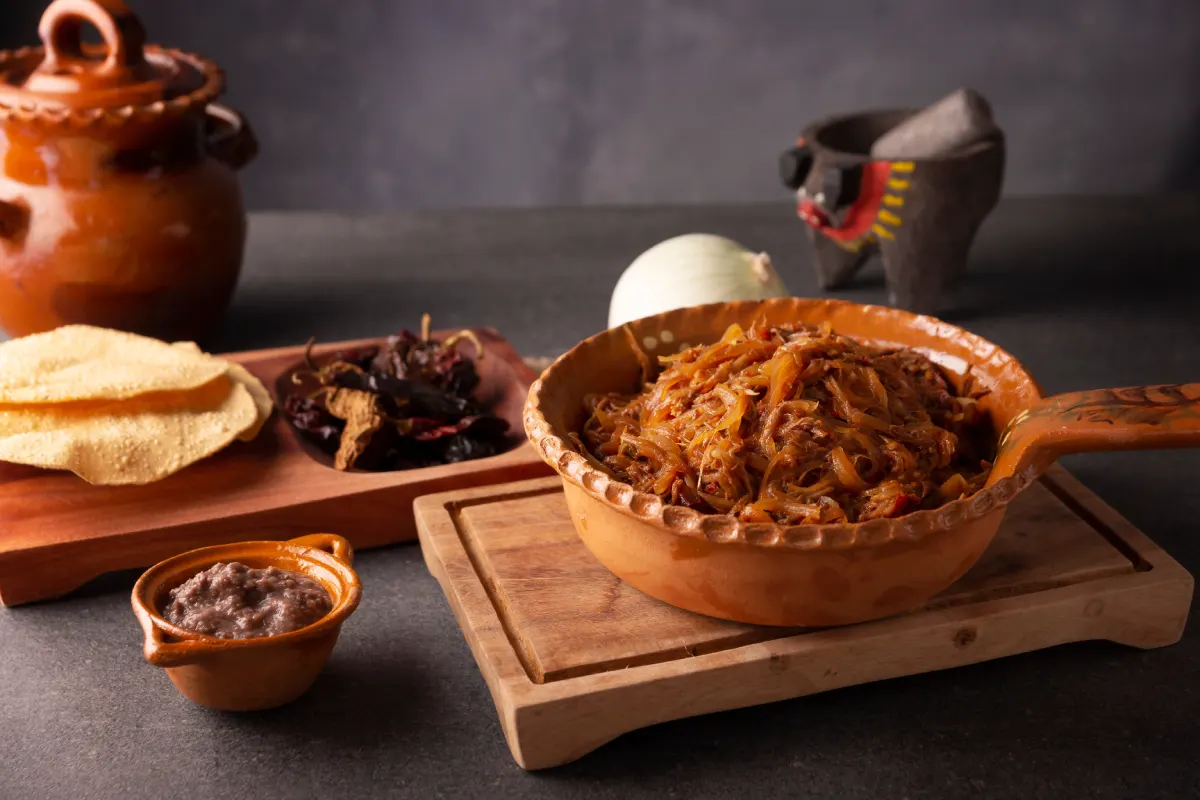 Mesa con ingredientes para preparar una tostada de tinga de res servida sobre una cazuela de barro