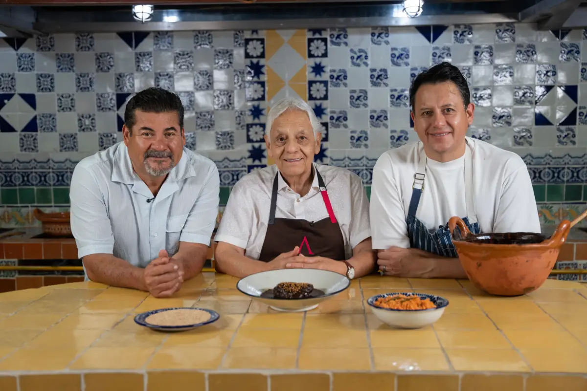 Hombres sonriendo junto con un plato de mole