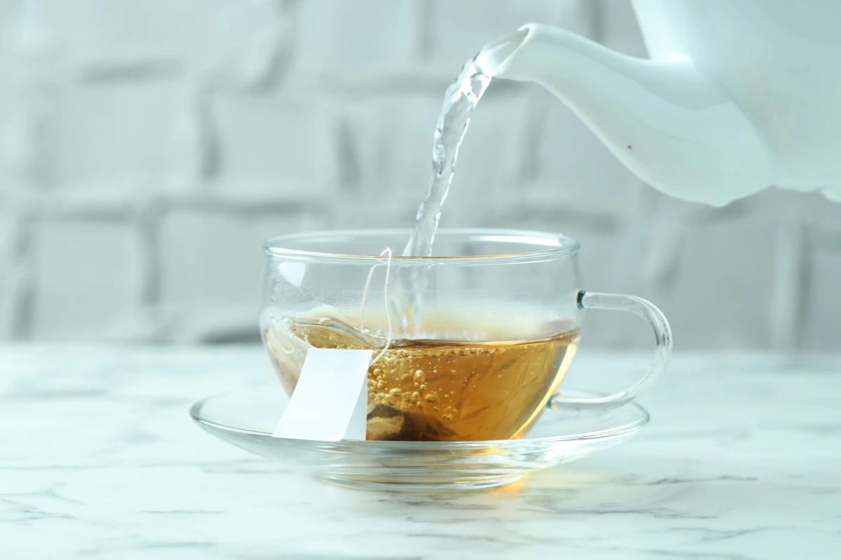 Taza con té vertiendo agua caliente