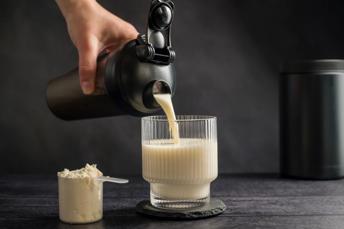 Persona sirviendo en vaso un batido de proteína blanco