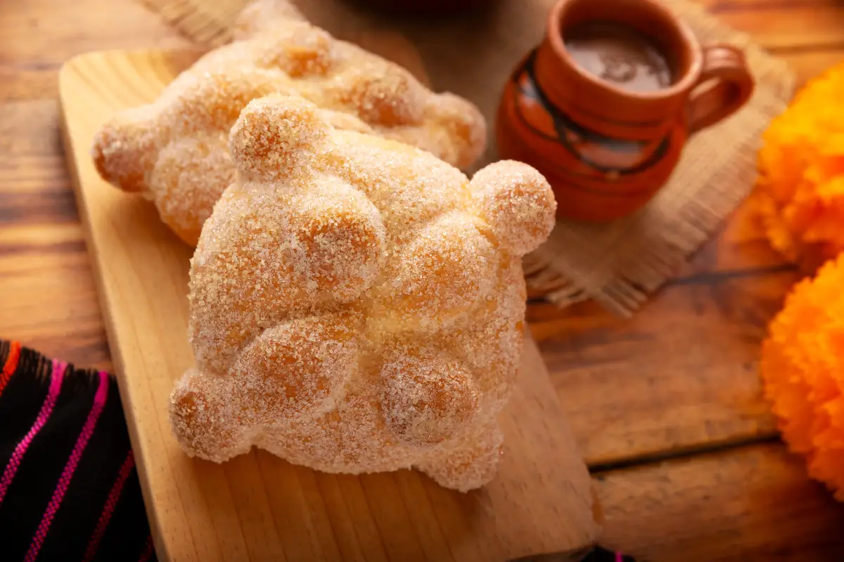 Dos piezas de pan de muerto acompañado con una bebida caliente