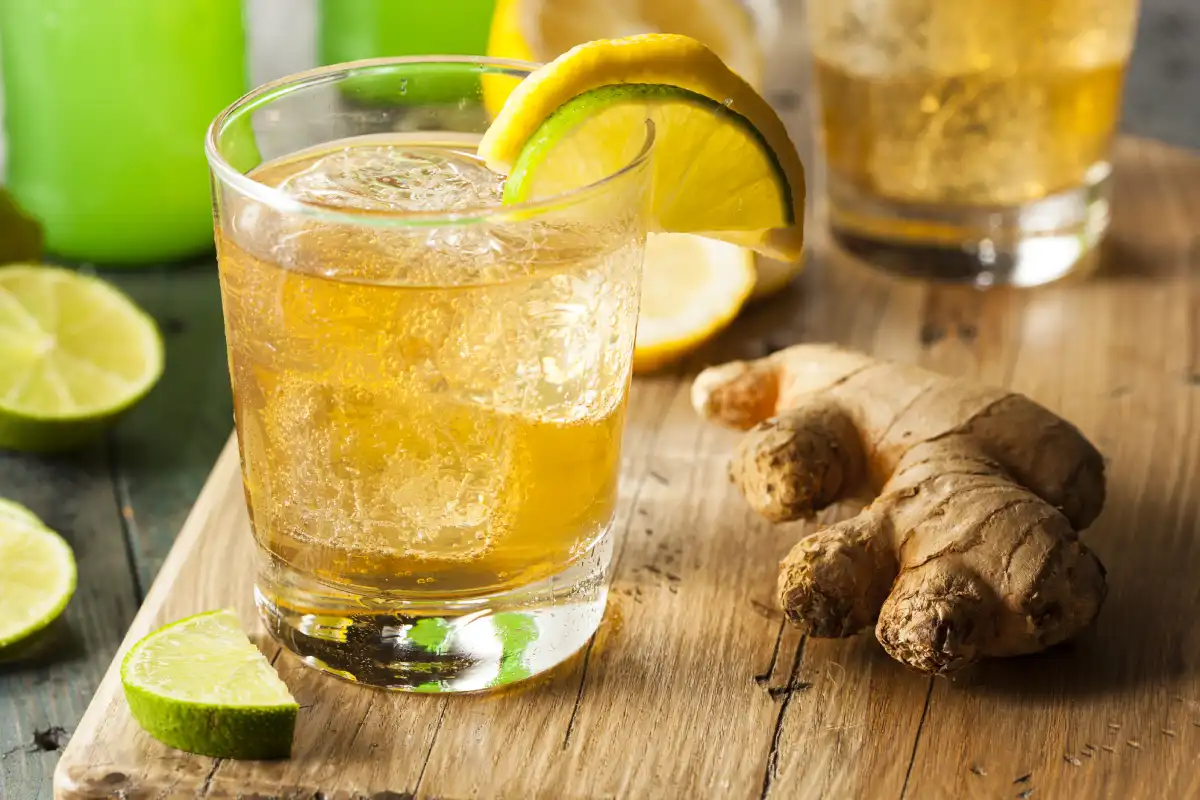 Un vaso con girger ale, rodajas de limon y una raiz de jengibre