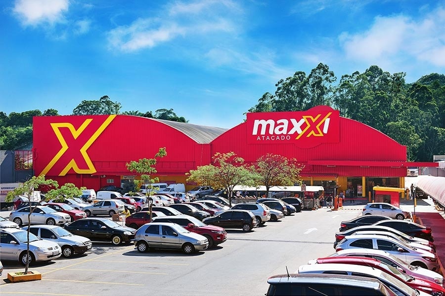 Frente da loja Maxxi Taboão. Em frente a loja, o estacionamento com diversos carros. Na fachada da loja escrito "Maxxi" e ao lado um grande "X" em destaque