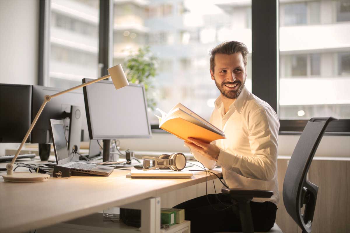 A smiling male office worker sitting at a desk in a modern office.